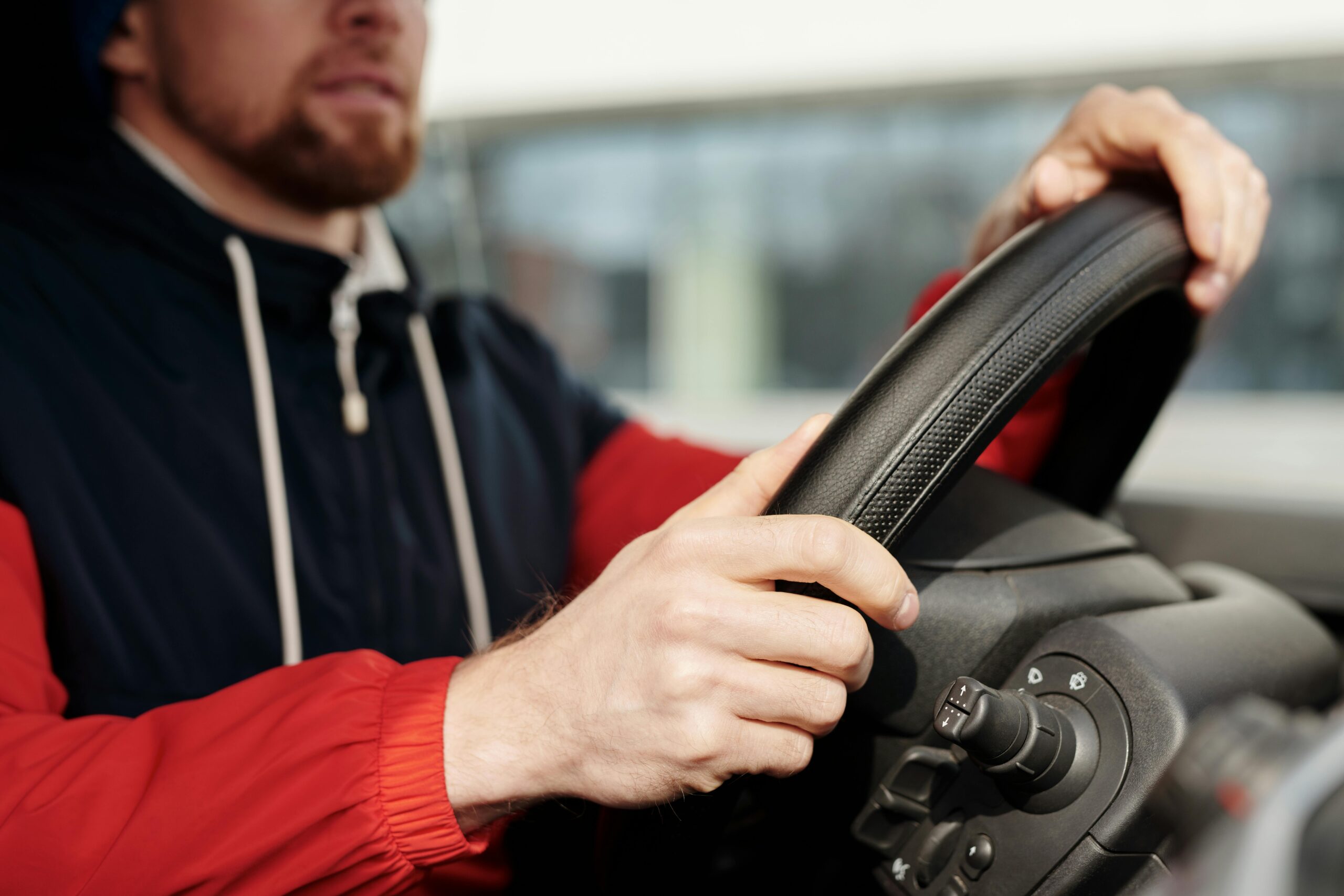 Focused man holding steering wheel, driving in vehicle interior. Close-up view with selective depth.