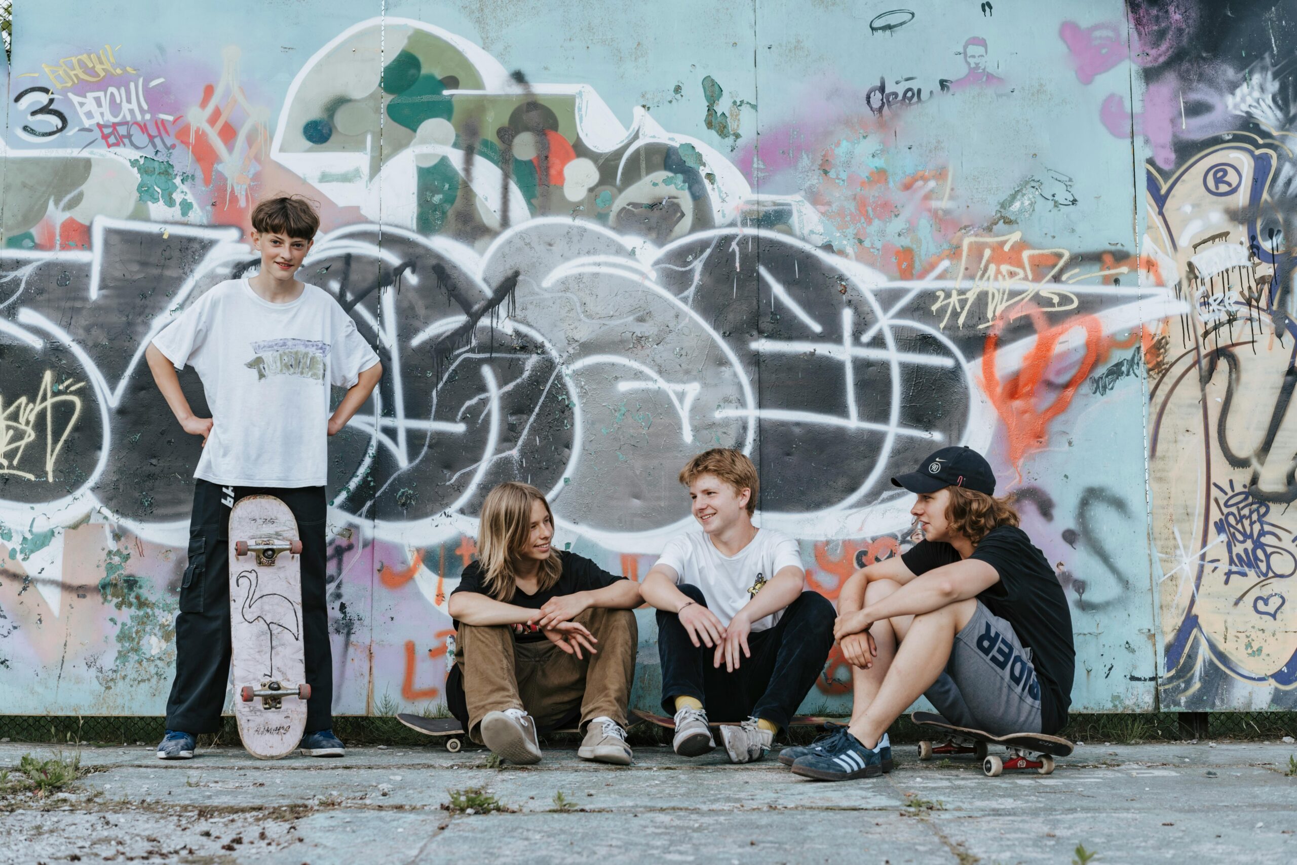 Four teenagers enjoying a casual skateboarding hangout in front of a vibrant graffiti-covered wall.