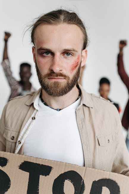 Serious bearded man with bruise holding a cardboard sign during a protest for human rights.